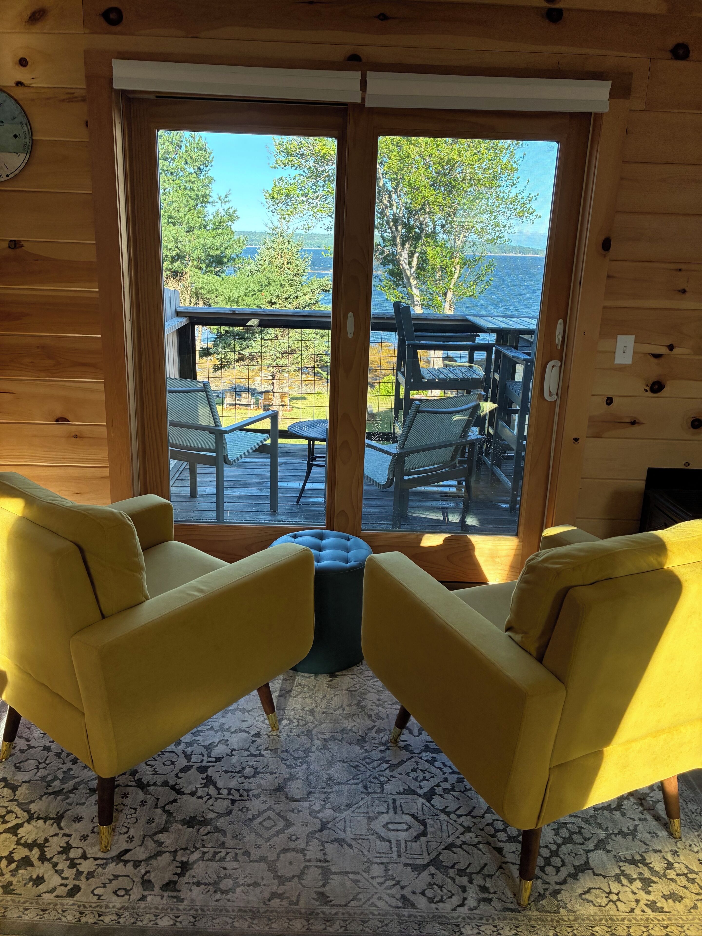 A wooden interior with two yellow armchairs facing a sliding glass door leading to an outdoor deck.