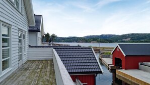 Ein Ufergrundstück mit Holzterrasse, einem roten Gebäude und Blick auf einen See und Hügel.