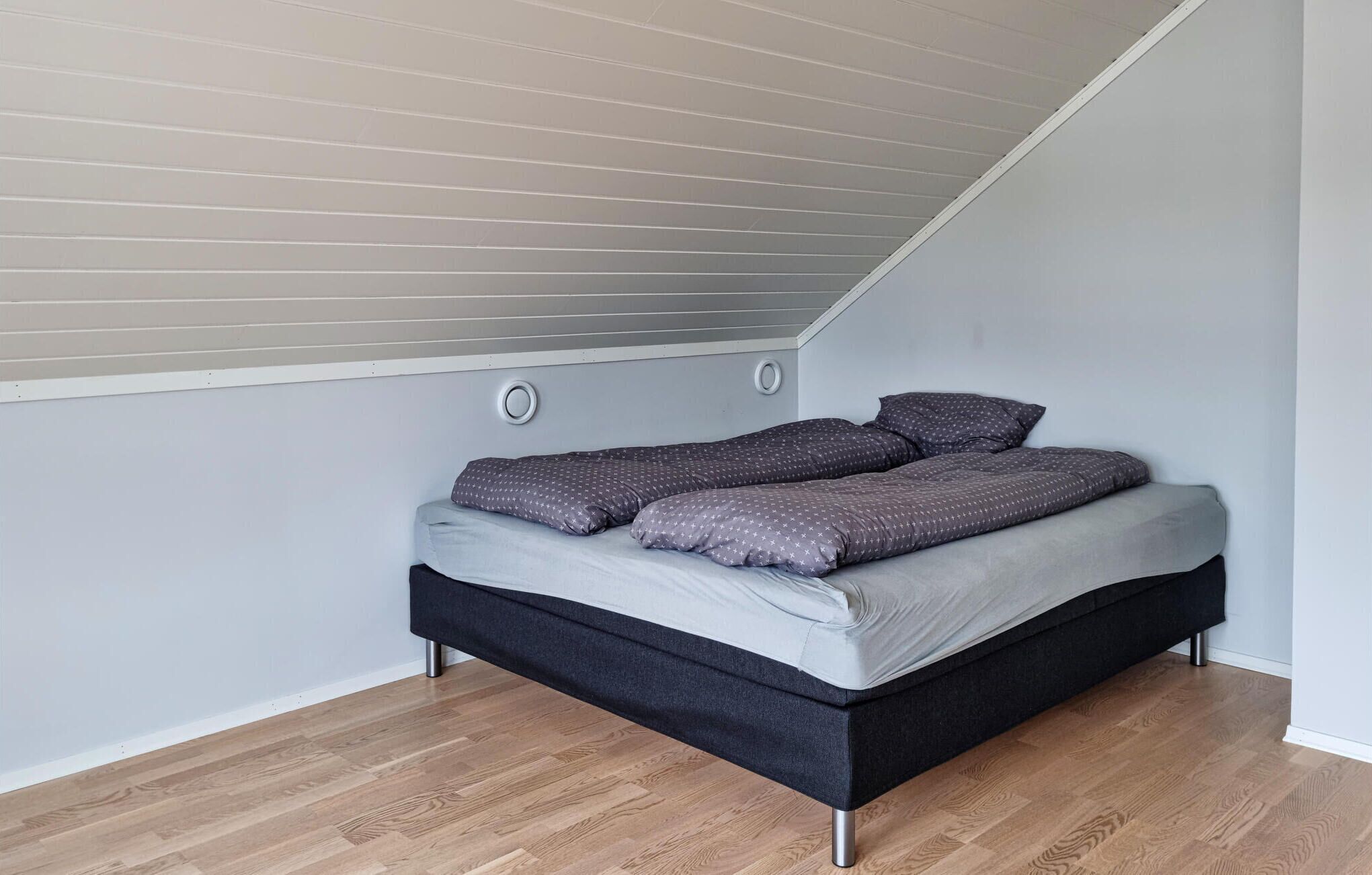 A compact bedroom with a sloped ceiling, a bed with grey bedding, and a wooden floor.