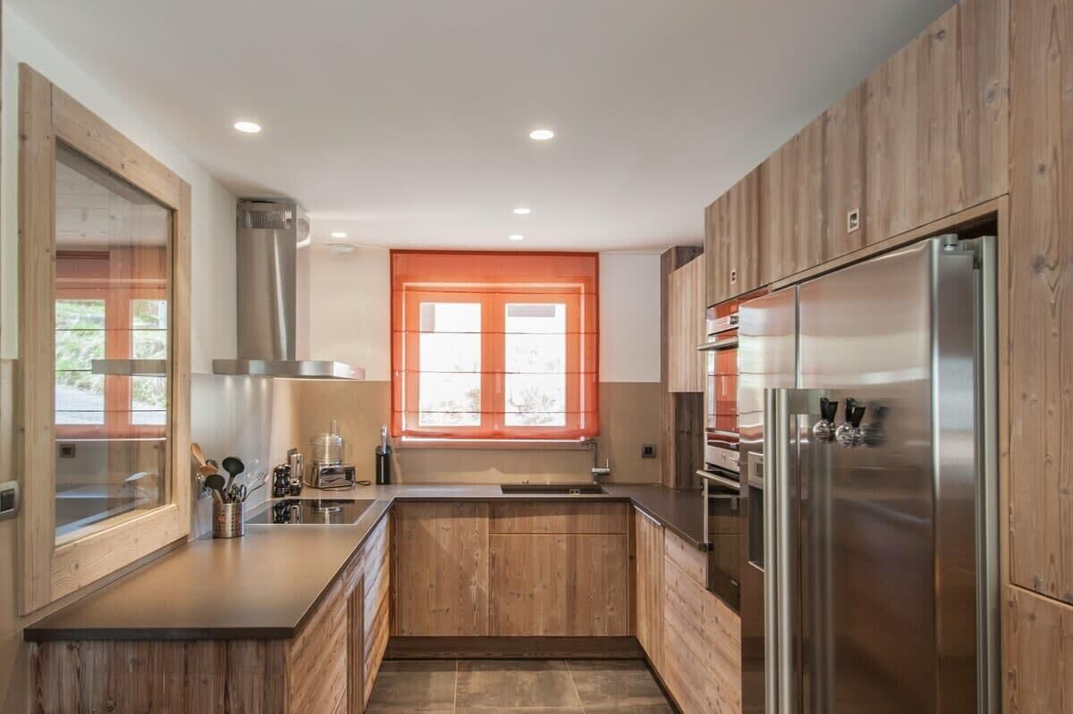 Una cocina moderna con armarios de madera, electrodomésticos de acero inoxidable y una ventana con persianas naranjas.