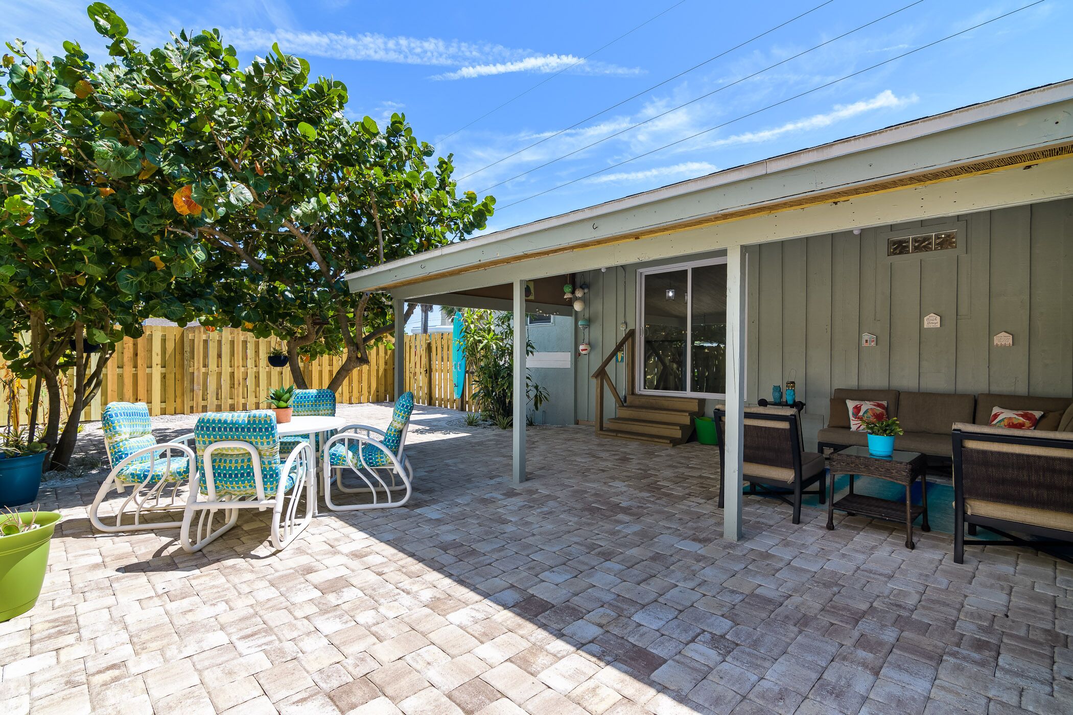 A covered patio with a brick floor, outdoor furniture, and a wooden fence.