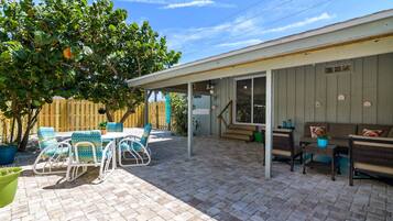 A covered patio with a brick floor, outdoor furniture, and a wooden fence.