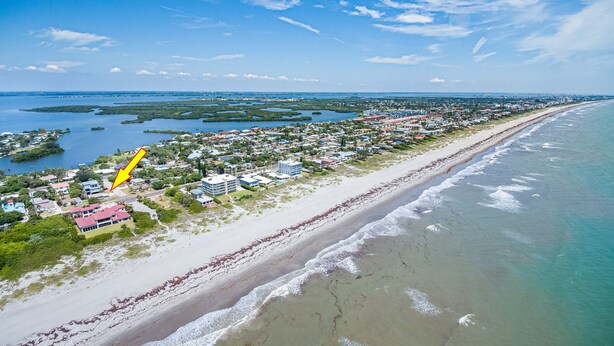Vista aérea de una zona costera con playa, edificios residenciales y un puerto deportivo.