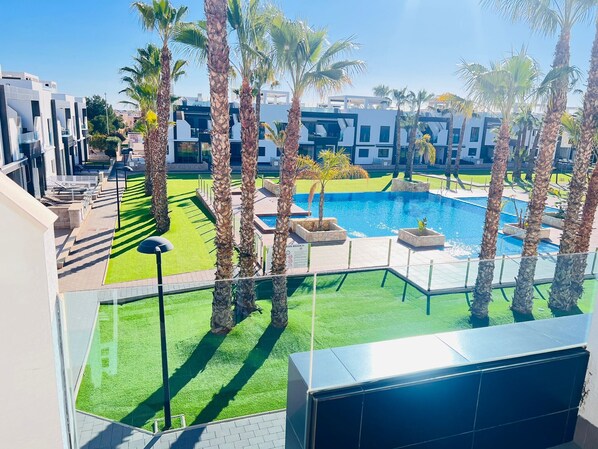 A modern hotel with a swimming pool, palm trees, and a well-maintained lawn.