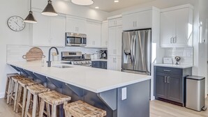 A modern kitchen with white cabinets, stainless steel appliances, and wooden stools. - Brand New | Pool | lazy river | Competition mini golf | RH (Washington)