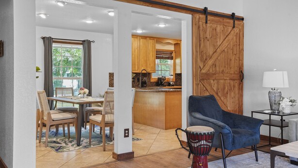 A modern living room with a dining area, a kitchen, and a sliding barn-style door.