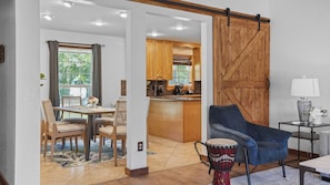A modern living room with a dining area, a kitchen, and a sliding barn-style door.