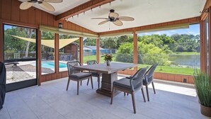 A covered patio with a table and chairs, a ceiling fan, and a view of a backyard with a pool.
