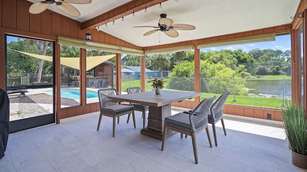 A covered patio with a table and chairs, a ceiling fan, and a view of a backyard with a pool.