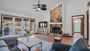 A spacious living room with a fireplace, a television, and a ceiling fan.