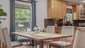 A dining area with a wooden table, woven chairs, and a view of the kitchen in the background.
