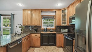 A kitchen with wooden cabinets, granite countertops, a built-in oven, a refrigerator, and a window with a view of the outdoors.