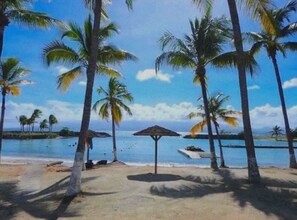 A beach with palm trees, a small boat, and a thatched umbrella. - Ti punch waterfront apartment with pool (Le Gosier)