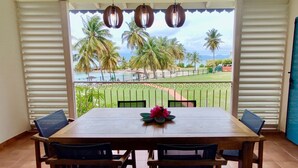 A dining area with a table and chairs, a flower centerpiece, and a view of palm trees and a beach.