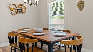 A dining area with a wooden table and chairs, a chandelier, and wall art. - New home w/hot tub, fireplace, firepit - Less than 1/2 mi to Main St. (Waynesville)