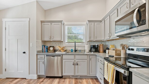 A modern kitchen with light gray cabinets, stainless steel appliances, and a wooden floor. - New home w/hot tub, fireplace, firepit - Less than 1/2 mi to Main St. (Waynesville)