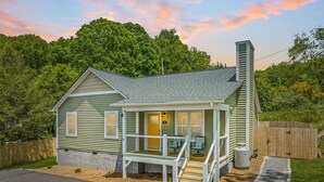 A small, single-story house with a porch, a chimney, and a fenced yard. - New home w/hot tub, fireplace, firepit - Less than 1/2 mi to Main St. (Waynesville)