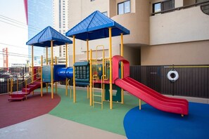 Um parquinho com escorregadores e estruturas de escalada, rodeado por um edifício com varanda.