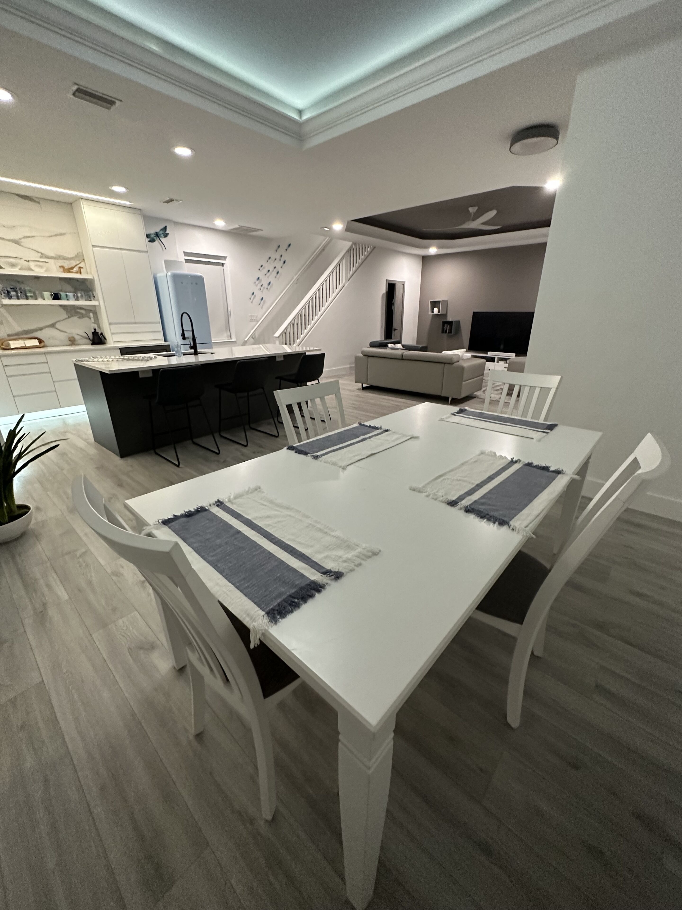 A modern kitchen with white cabinetry, a central island, and a dining area with a white table and chairs.