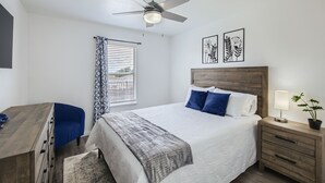 Une chambre à coucher comprenant un lit, une table de chevet, une commode et un ventilateur de plafond.