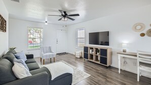 Un salon moderne avec un canapé gris, une table basse blanche, un téléviseur posé sur un meuble en bois et un ventilateur de plafond.