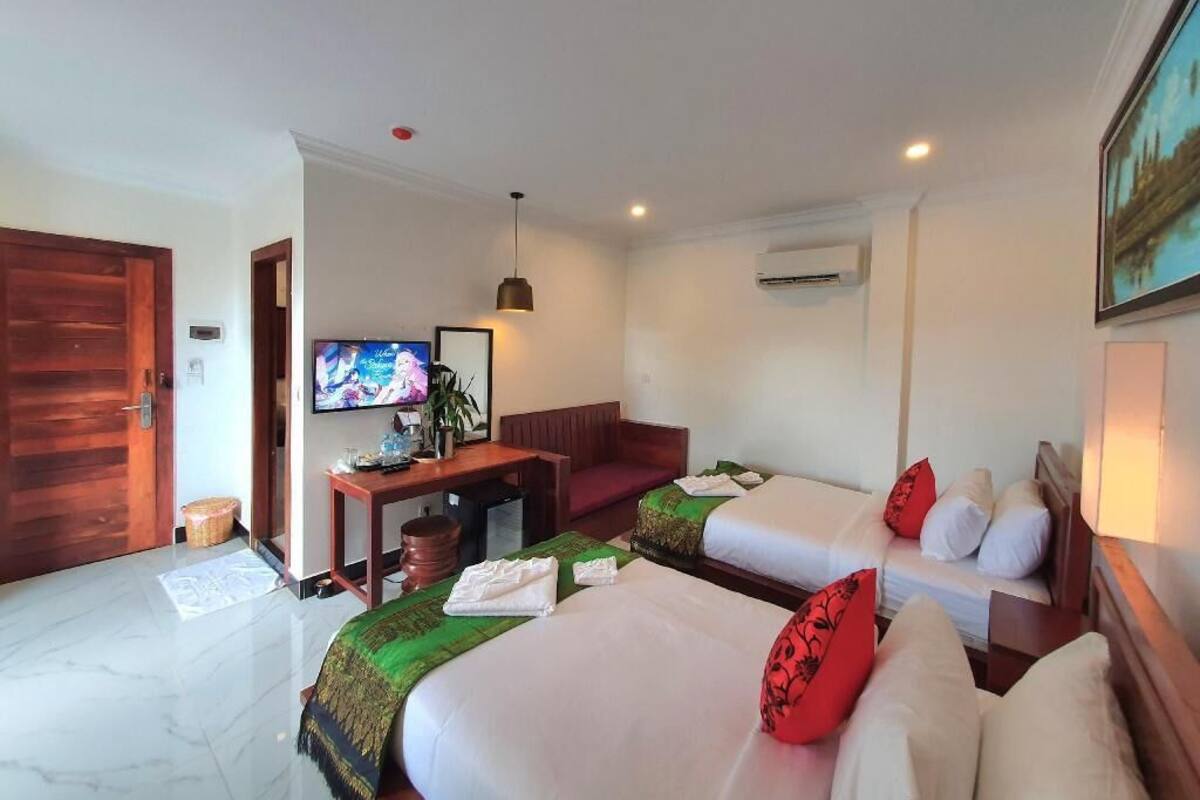 Ein Hotelzimmer mit zwei Betten, einem Schreibtisch, einem Fernseher und einer Klimaanlage.