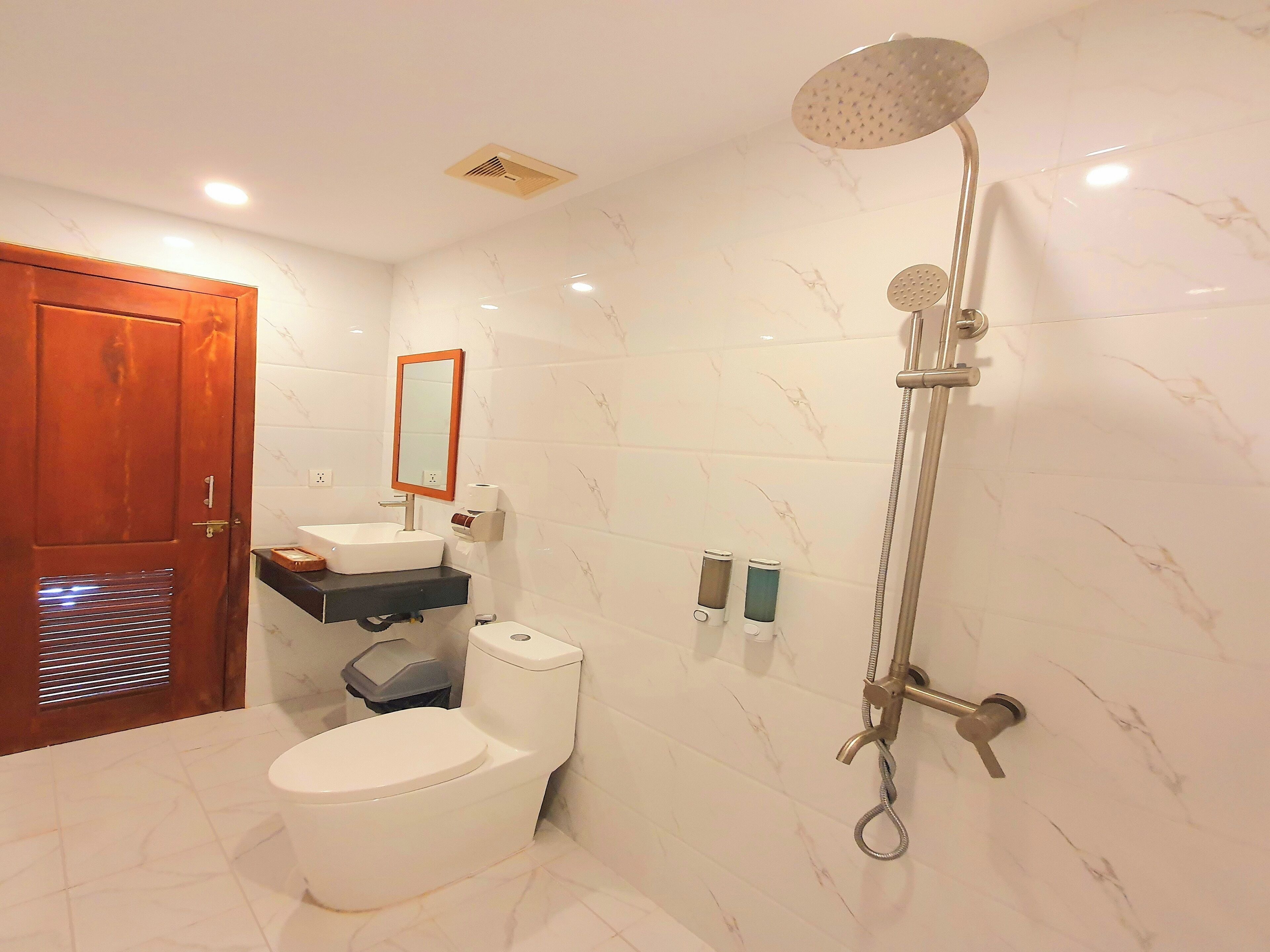 A bathroom with a toilet, sink, mirror, shower, and marble-tiled walls.