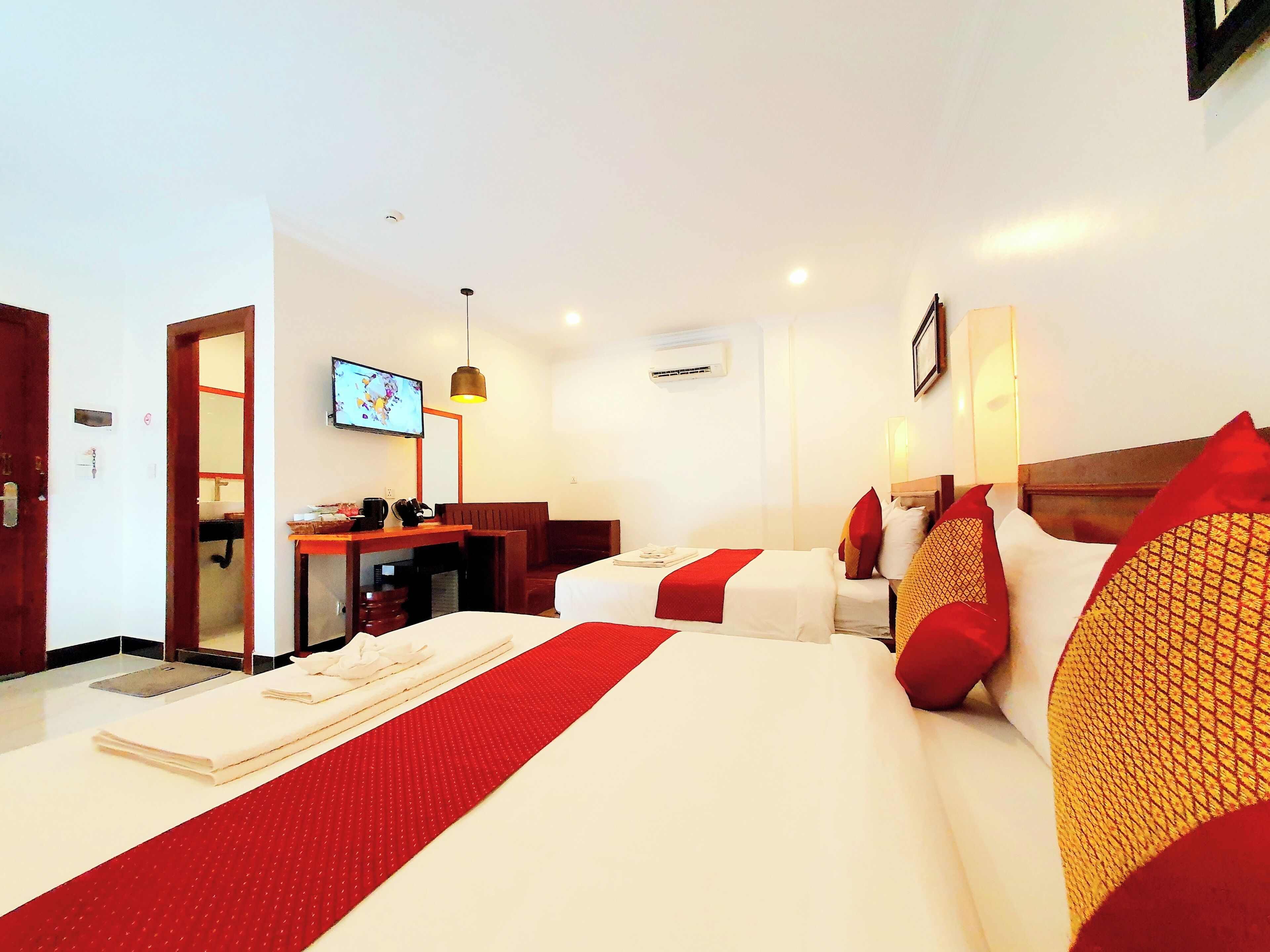 A hotel room with two beds, a desk, a TV, and a red accent wall.