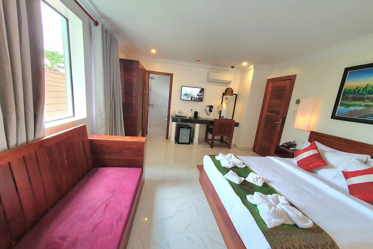 Ein Hotelzimmer mit Bett, Schreibtisch, Stuhl, Fernseher und einem Fenster mit Vorhängen.