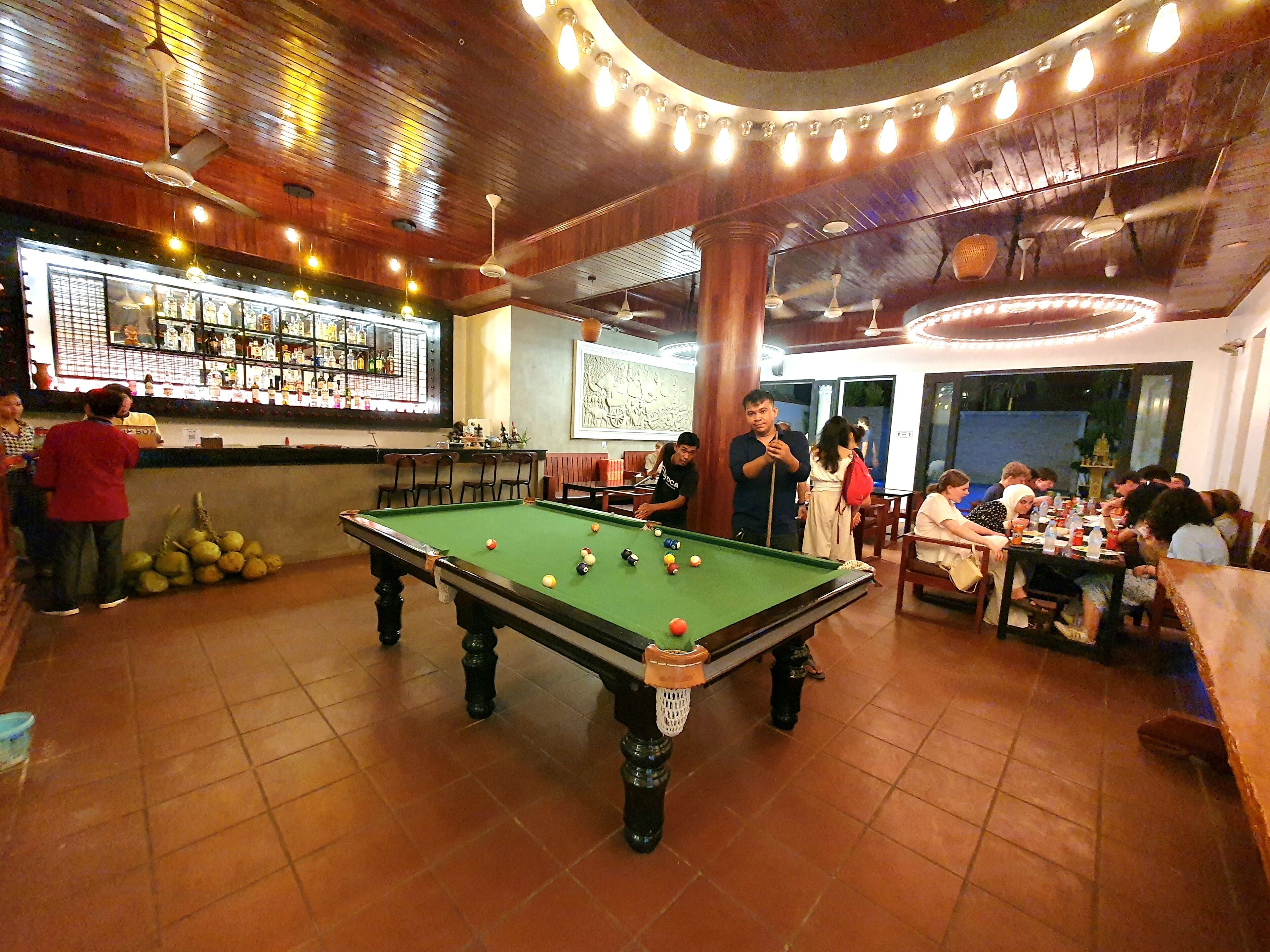 Una mesa de billar en una sala con bar y zona de estar.