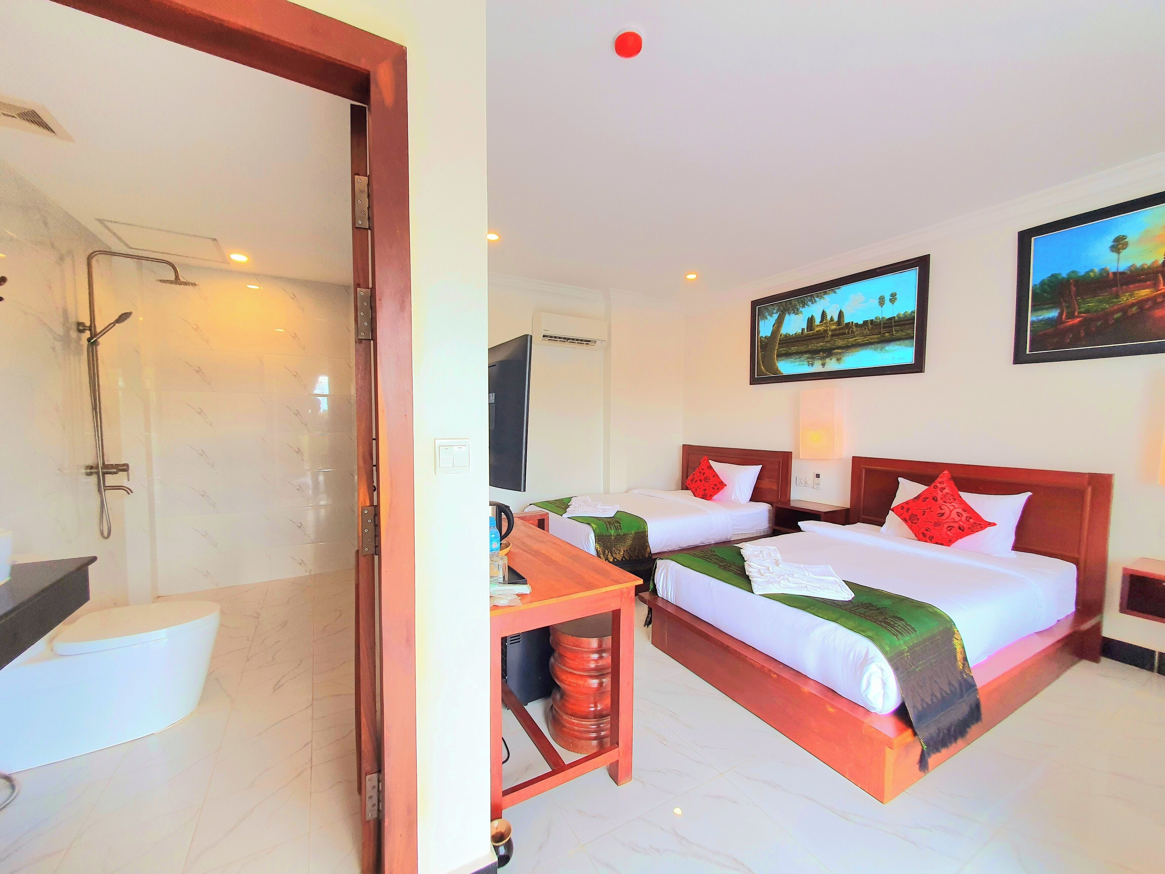 Ein Hotelzimmer mit Dusche, zwei Betten, einem Fernseher und Kunstwerken an den Wänden.