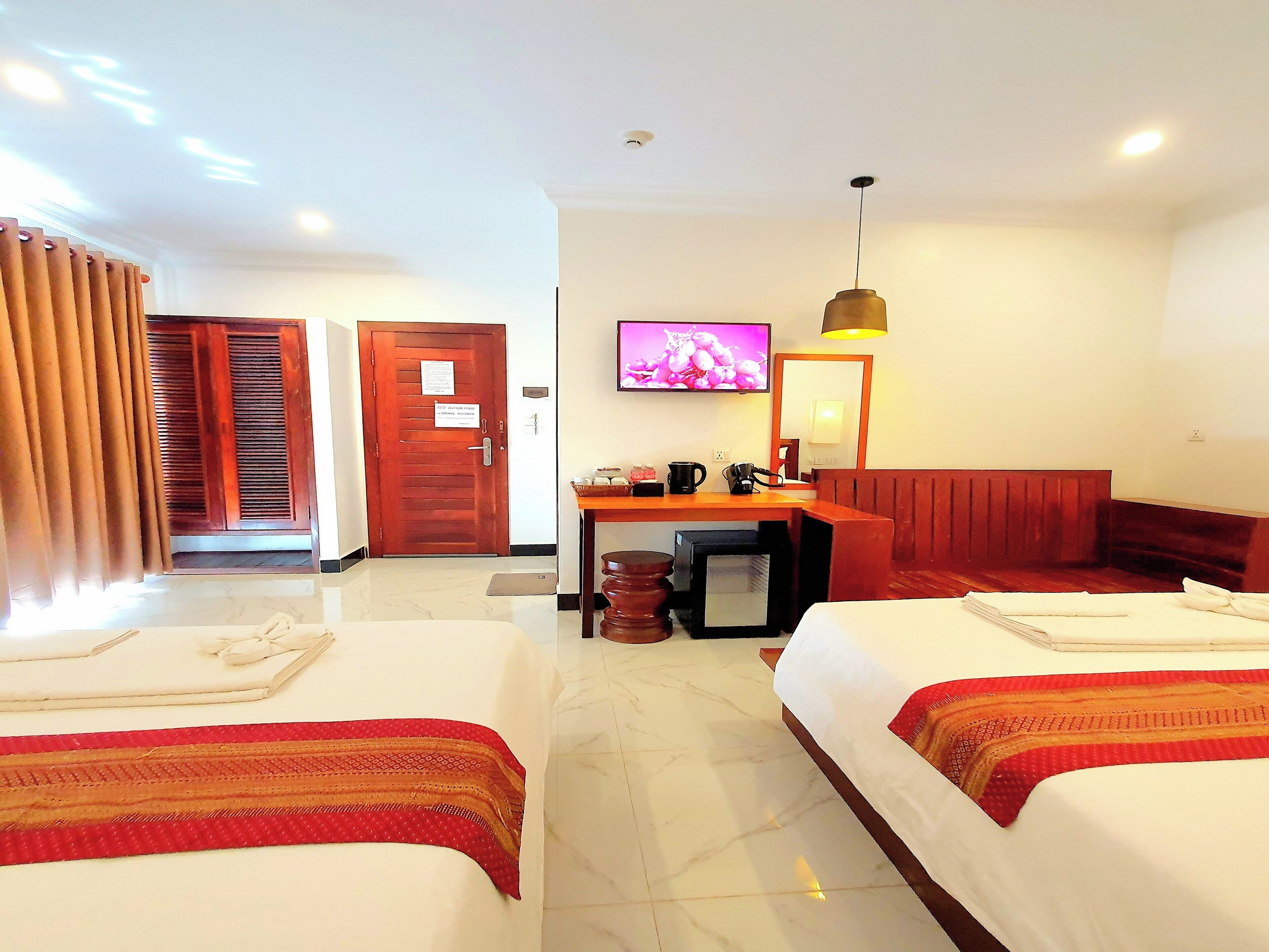 Habitación de hotel con dos camas, un escritorio con silla, televisión y un refrigerador pequeño.