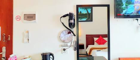 A hotel room with a bed, a TV, a mirror, a coffee maker, and a kettle on the counter.