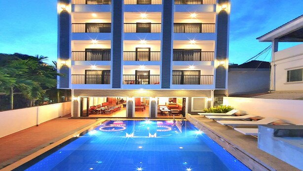 Ein mehrstöckiges Hotel mit Swimmingpool, Außenbereich zum Sitzen und Balkonen.