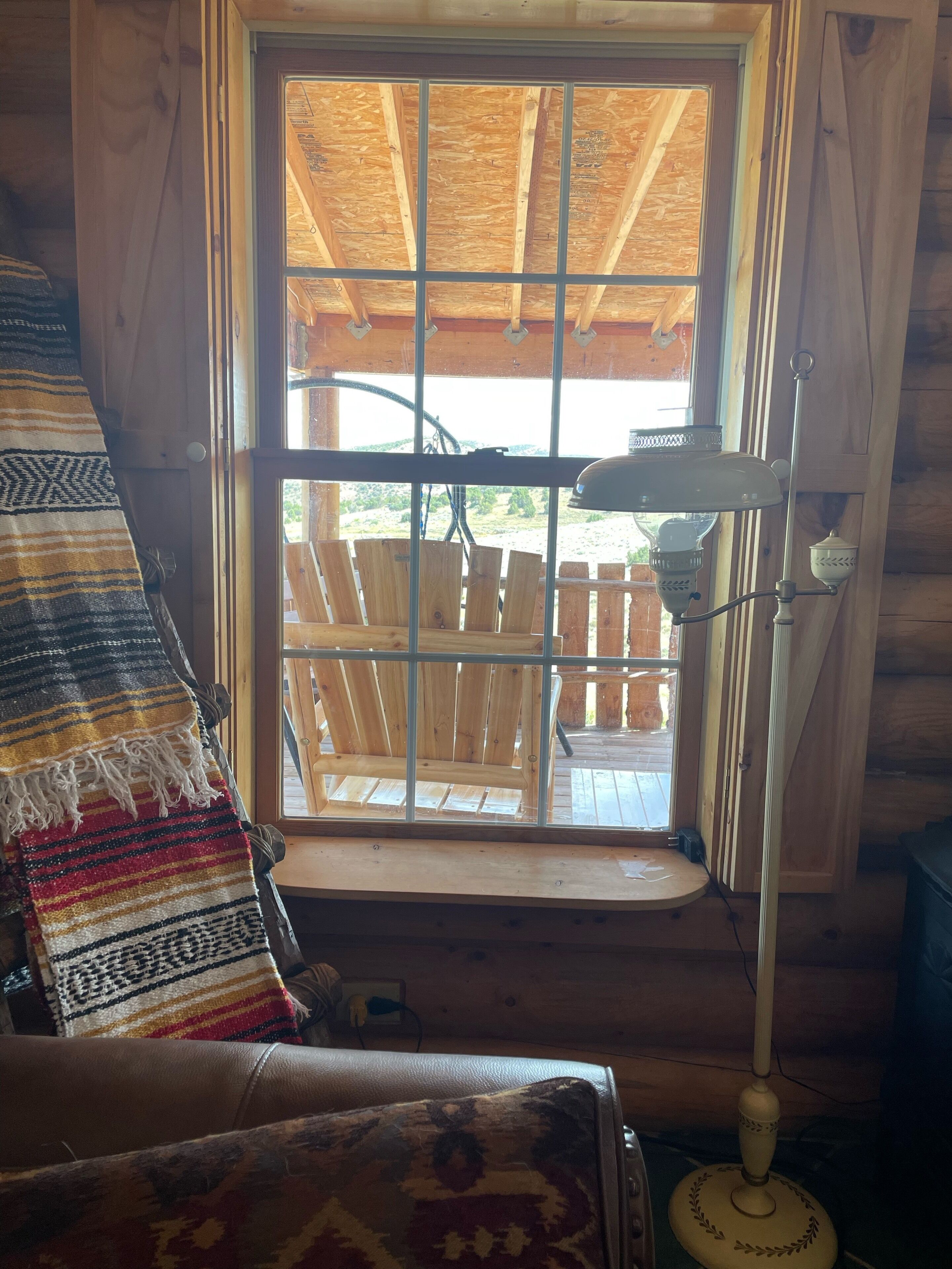 A wooden cabin interior with a window overlooking a wooden deck.