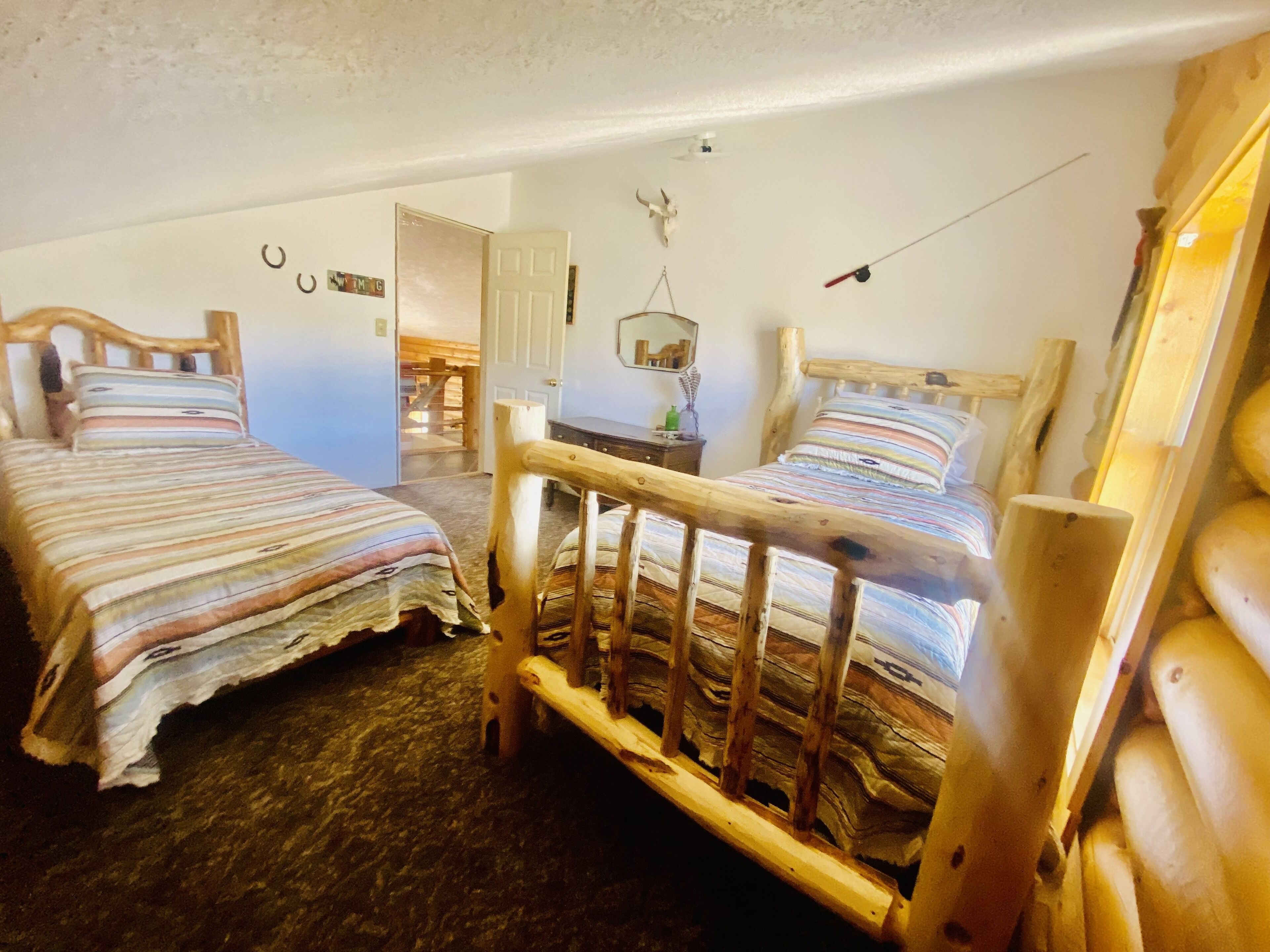 Una habitación acogedora con dos camas de madera, una mesita de noche de madera y una decoración rústica que incluye un cráneo de vaca y una lámpara colgante.