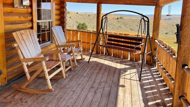A wooden deck with rocking chairs and a swing, overlooking a desert landscape.