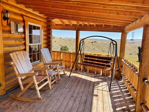 A wooden deck with rocking chairs and a swing, overlooking a desert landscape.