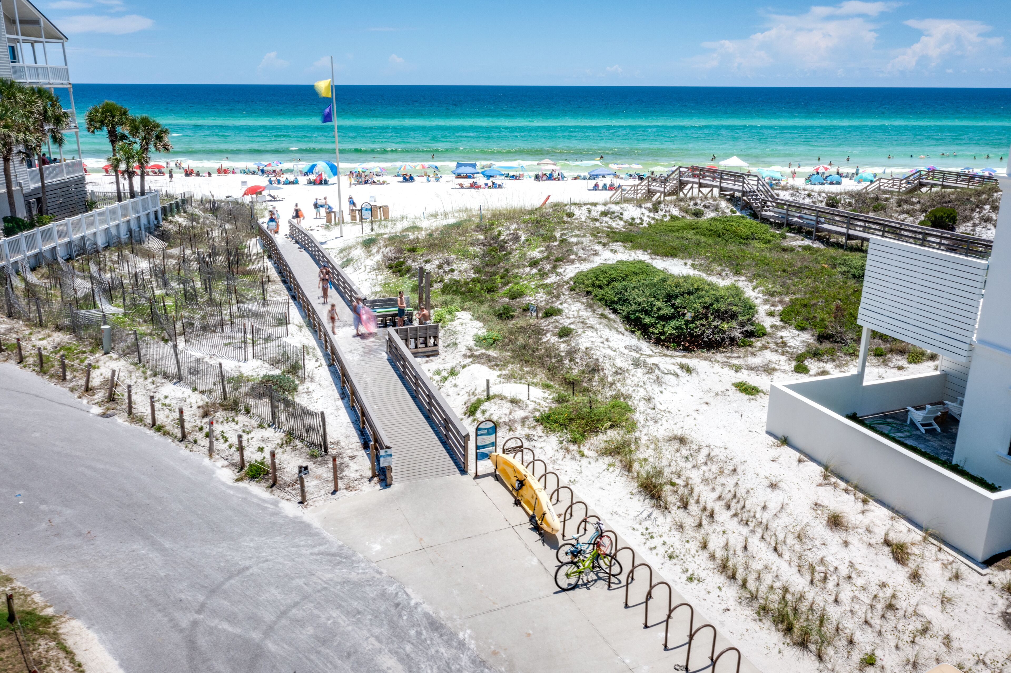 Vista de la playa con un paseo marítimo que lleva al agua, una torre de salvavidas y sombrillas de playa.