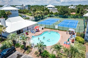 Relax by the pool surrounded by lush greenery and modern architecture, with lounge chairs and umbrellas providing ample shade.