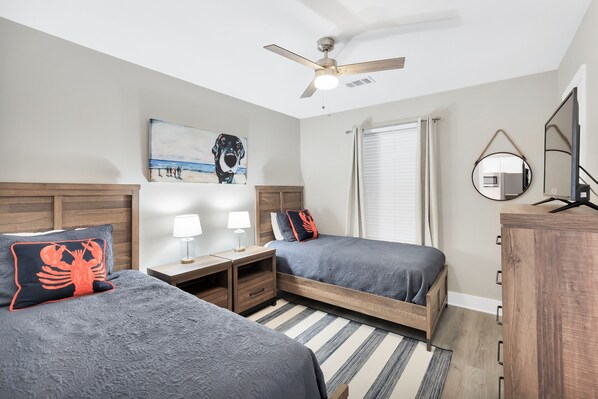 A bedroom with two beds, a ceiling fan, a painting, a window with curtains, a bedside table with a lamp, and a dresser. - Short walk or free shuttle to wide open public beach! 3BR/2BA (Santa Rosa Beach)