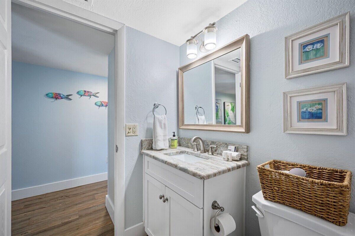 Une salle de bain avec un meuble-lavabo blanc, deux vasques, un miroir et un panier en osier posé sur les toilettes.