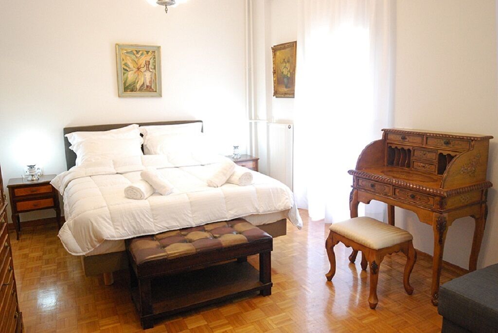 A bedroom with a large bed, a wooden bench, a nightstand, and a dresser.