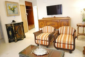 Un salon comprenant un téléviseur, deux fauteuils à rayures, un meuble en bois et une table basse en verre.