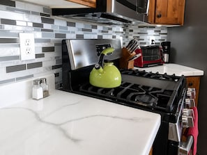 A kitchen with a stainless steel stove, a green kettle, a red toaster, and a white countertop. - The Good Life (Cedar City)