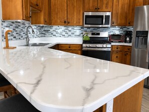 A kitchen with a marble countertop, stainless steel appliances, and wooden cabinets. - The Good Life (Cedar City)