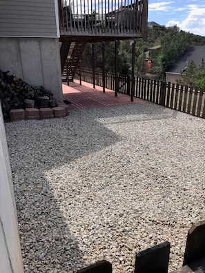 A gravel patio area with a wooden deck and a metal railing. - The Good Life (Cedar City)