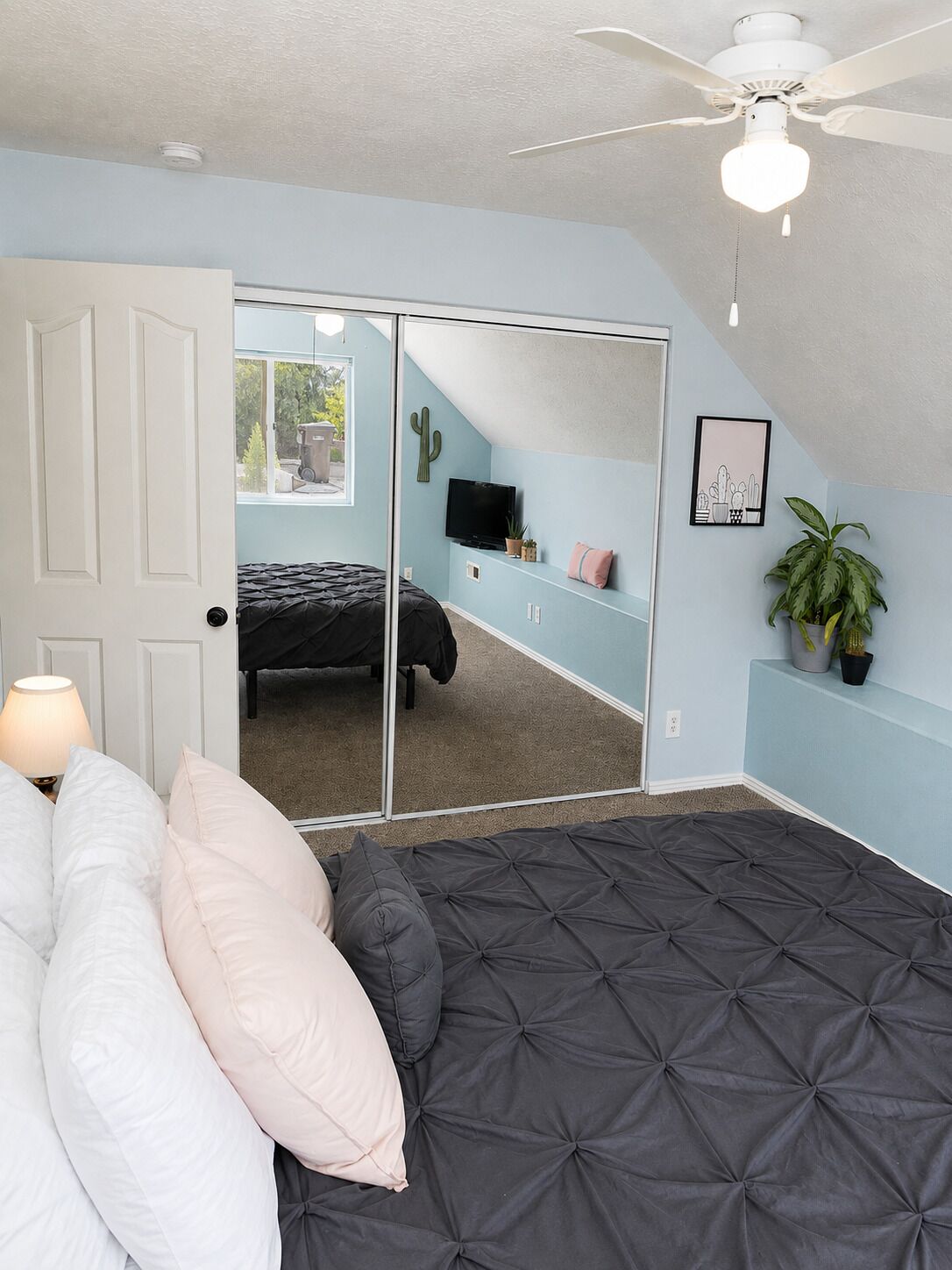 Un dormitorio con cama, ventilador de techo, televisor y puerta corredera que da a un balcón.