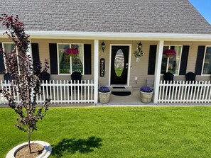 A two-story house with a white picket fence, a front porch with chairs, and a welcome sign. - The Good Life (Cedar City)