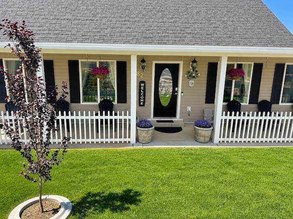 A two-story house with a white picket fence, a front porch with chairs, and a welcome sign. - The Good Life (Cedar City)